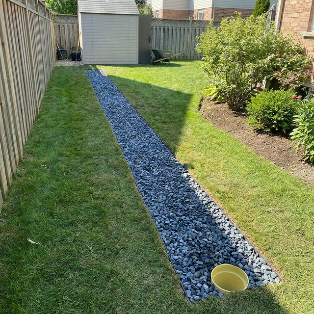 Completed French drain in a residential yard showing a linear gravel trench extending across a green lawn